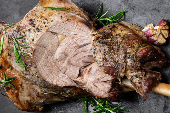 Whole roast lamb leg on black stone background