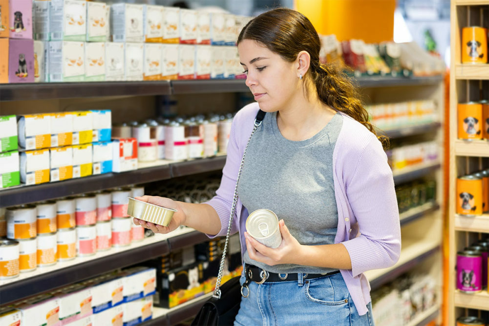 Woman in grocery store pet food aisle reading label on a can