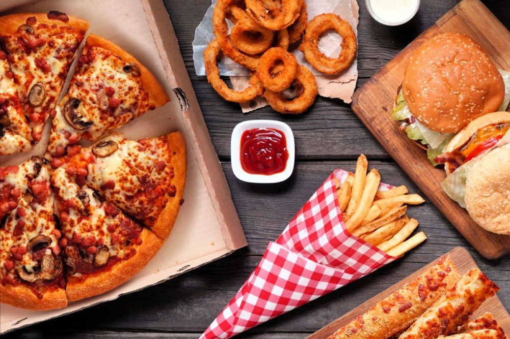 Pizza, fries, onion rings and burger laid out on table