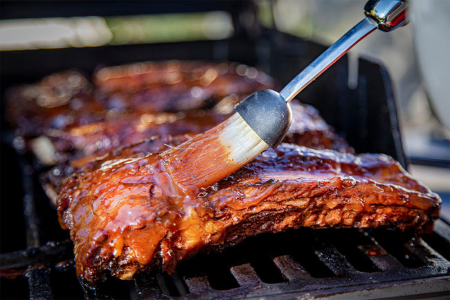 Beef ribs being basted with BBQ over grill