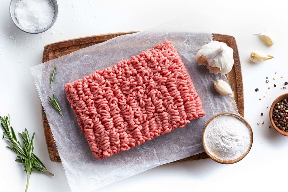 ground beef on cutting board with rosemary, garlic and seasoning