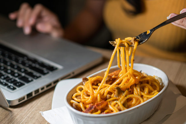 Working on a laptop while eating a bowl of spaghetti