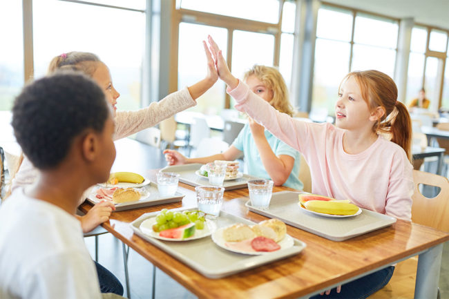 Kids high-five while having lunch at school cafeteria