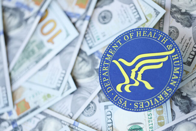 The US Department of Health and Human Services logo laying over several $100 bills